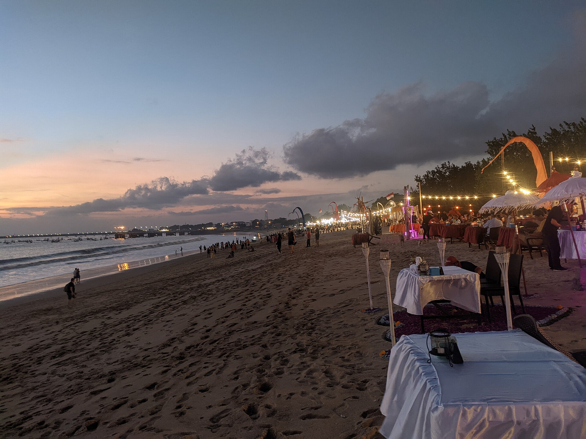 Beachfront seafood restaurants along the sand at Jimbaran, Bali, during a golden sunset