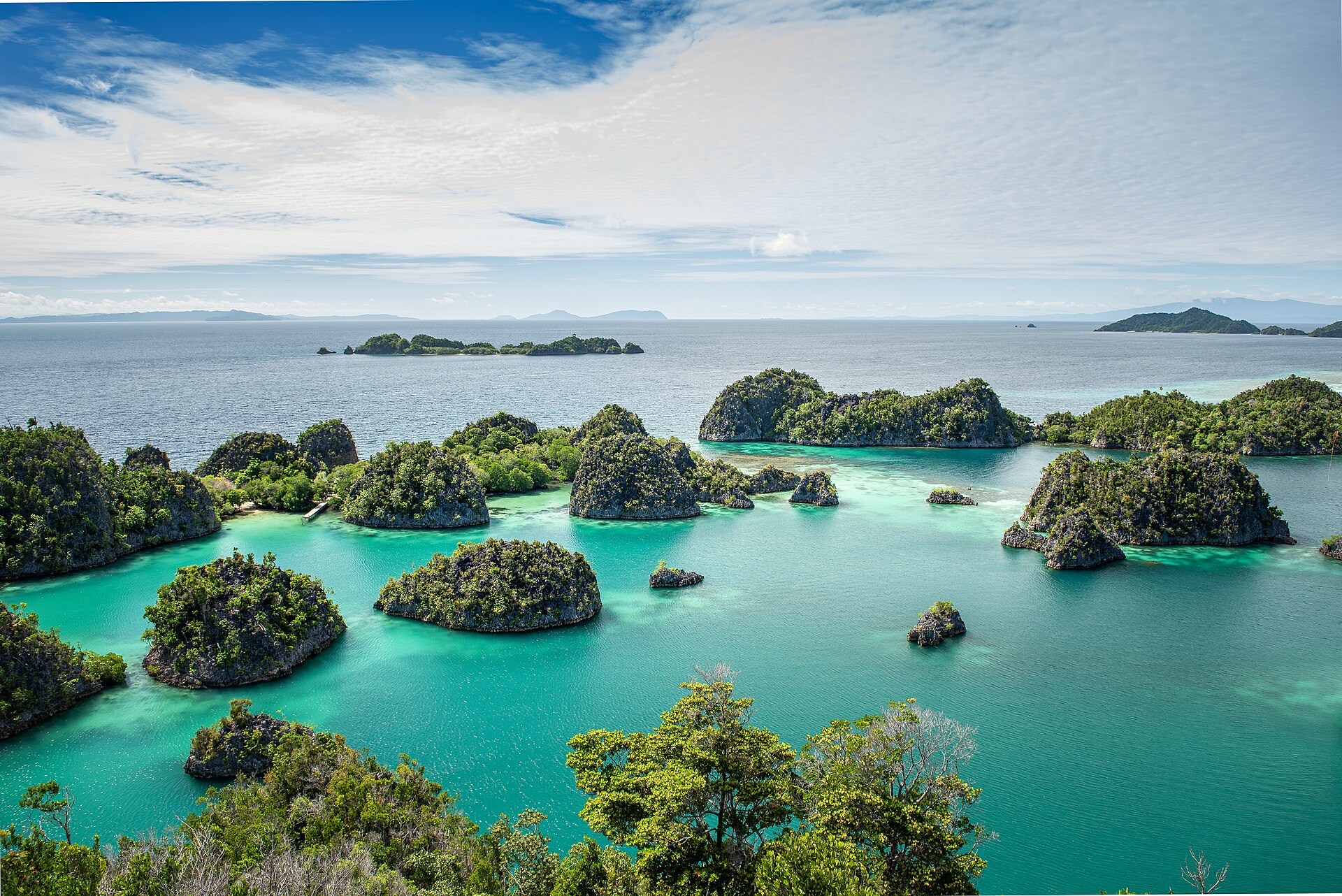 Green karst islets rising from bright turquoise water under blue sky at Piaynemo, Raja Ampat